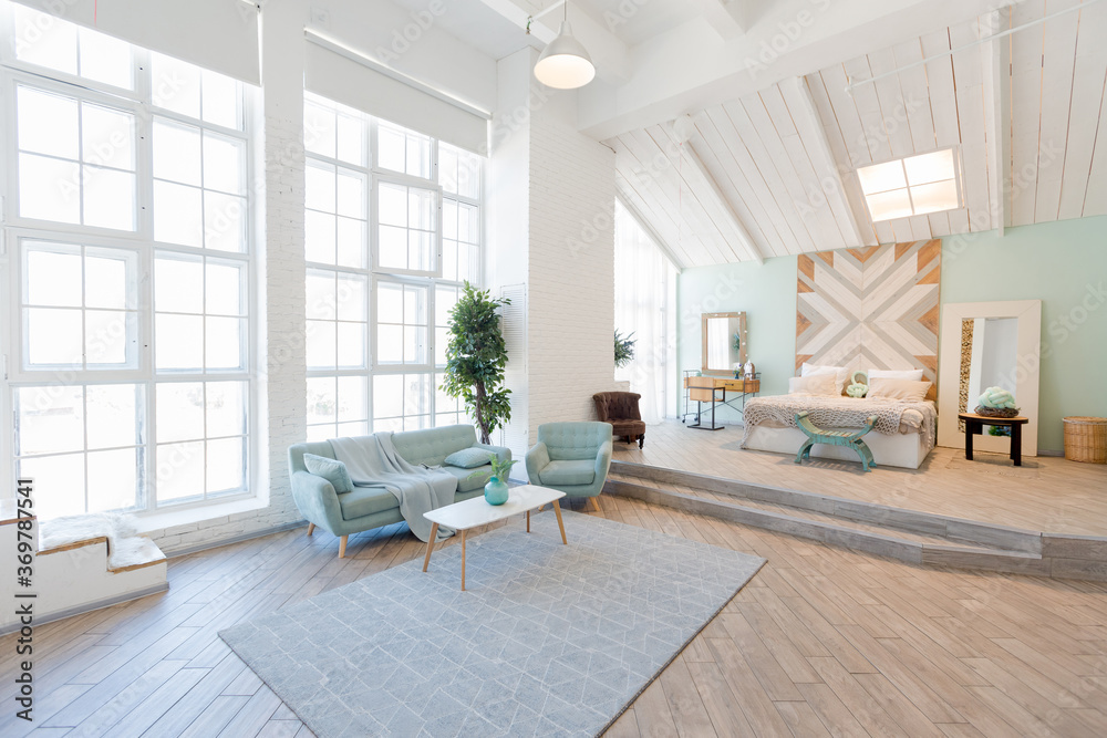 Fototapeta premium Fashionable spacious apartment with a stylish design in green, grey and white pastel colors with big window and decorative walls. bedroom and kitchen space