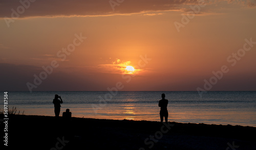 Tourists at sea on the beach, admire the sunrise. Silhouettes of people