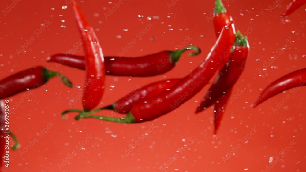 Super slow motion of coloured chilli peppers in collision, red background. Filmed on high speed cinema camera, 1000 fps