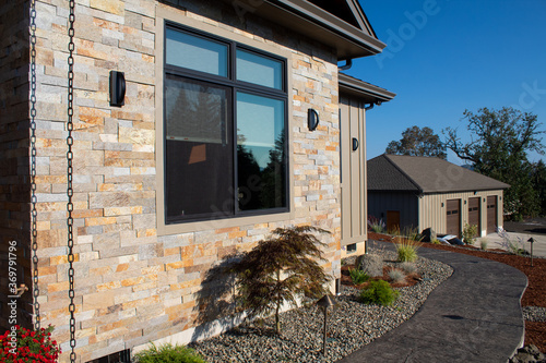 Landscape plants and rocks by a modern house with stone veneer siding.