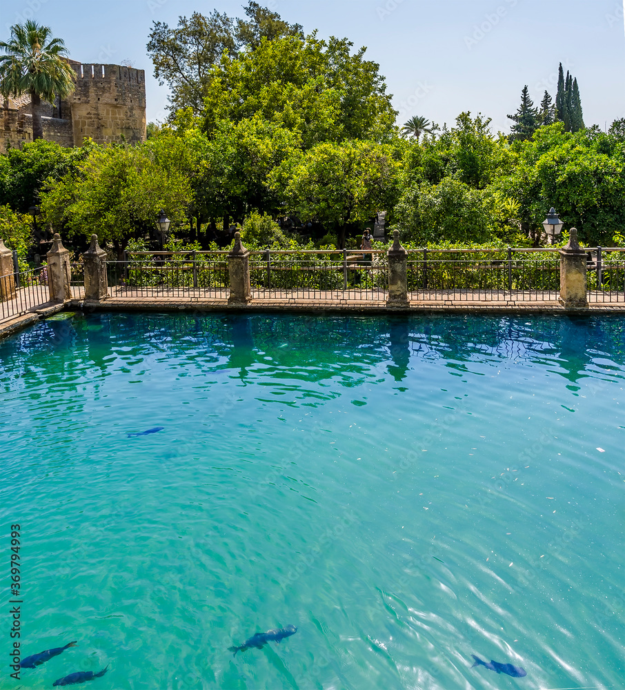 Ornamental fish ponds and wooded gardens leading to old town fortifications in Cordoba, Spain in the summertime
