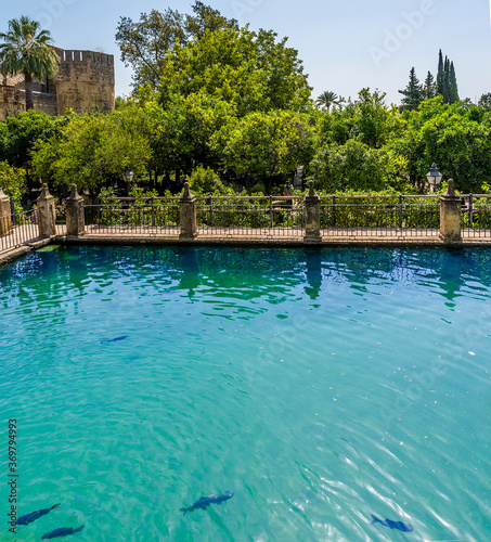 Ornamental fish ponds and wooded gardens leading to old town fortifications in Cordoba, Spain in the summertime