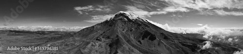 Black and white panarama of the vulcano Chimborazo that has a white top covered in snow and shows five of the mountain ridges