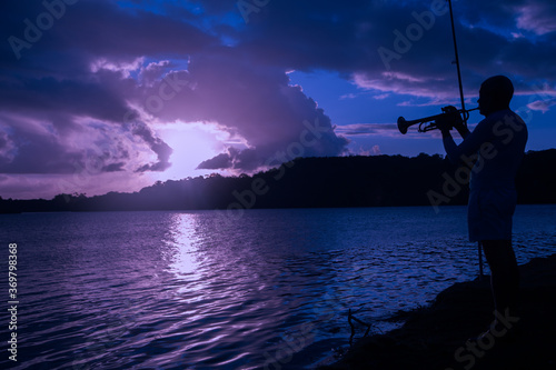 silhouette of a man playing trumpet and fishing at lake shore