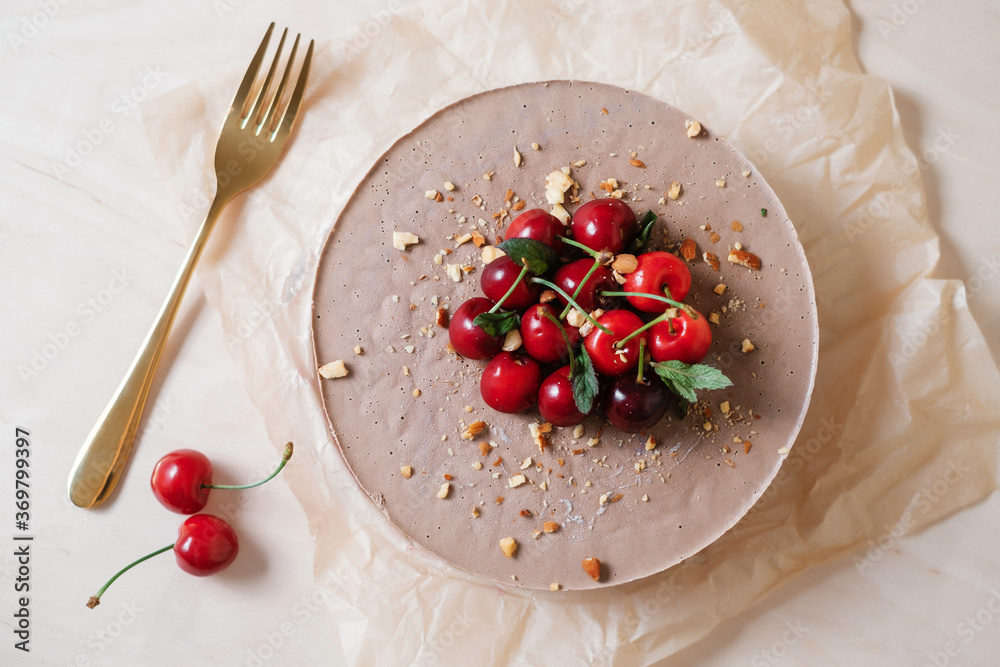 Homemade chocolate cake with cherry on parchment paper. Food delivery. Homemade baking. Top view. Delicious tart with chocolate and cherry on the wooden with golden fork.
