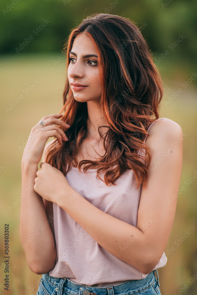 Portrait of beautiful sexy young woman with long brown hair in pink tank top and denim shorts posing outdoors, sensual, serious Portrait of beautiful sexy young woman with long brown hair in pink tank top and denim shorts posing outdoors, sensual, serious