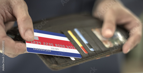 Pulling plastic bank card with flag of Costa Rica out of the wallet, fictional card number