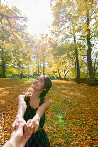 Fototapeta Naklejka Na Ścianę i Meble -  Young happy Asian woman smiling while leading man with both hands in the forest while looking up