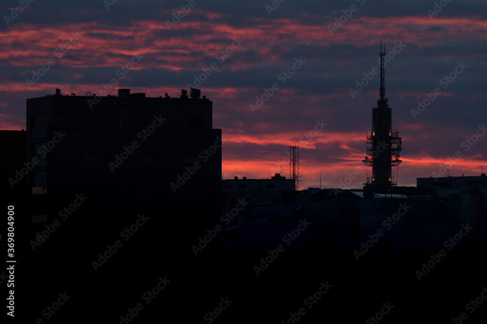 A silhouette of a tall telecommunication/broadcasting tower against the vivid red sky on a cloudy summer evening.