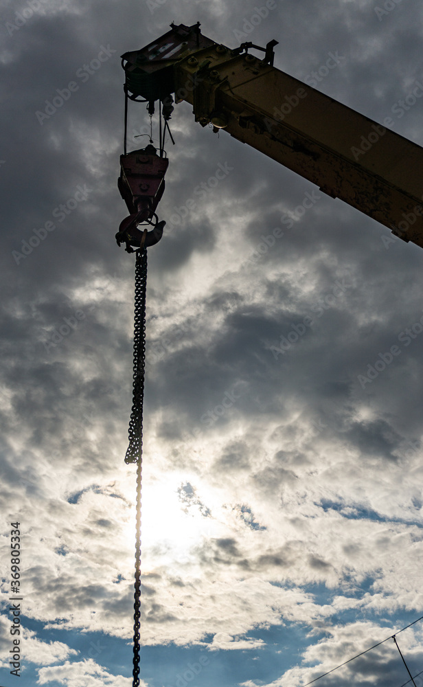 Crane with chain on a background of blue cloudy sky. Construction.