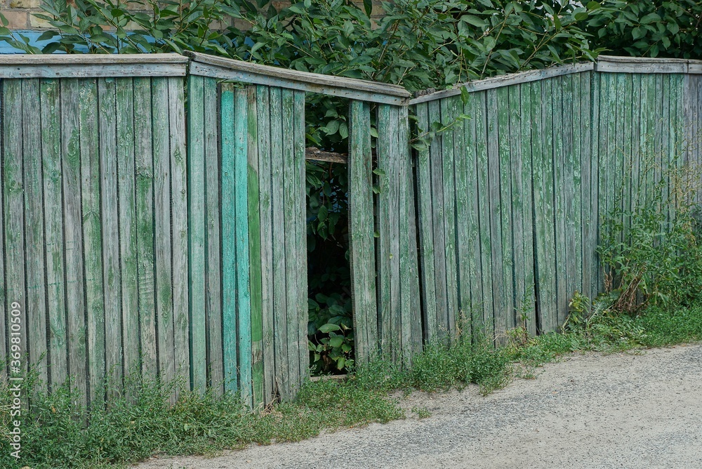 part of a green wooden old fence with broken boards on a rural street