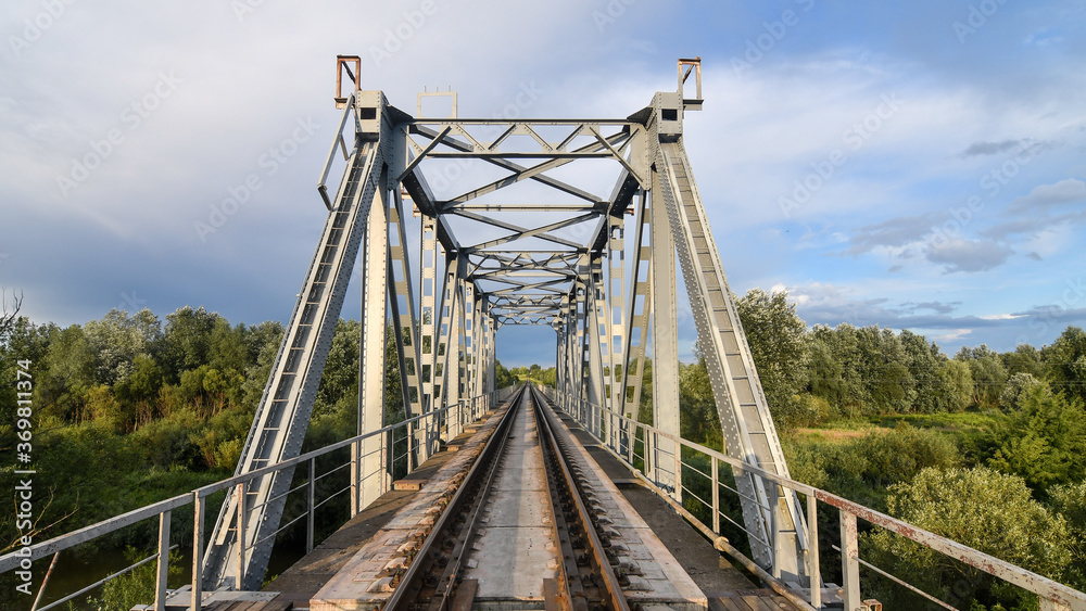 Big metal railway bridge over the river at sunset in summer.