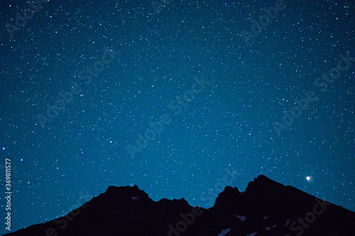 Stars dot the night sky above the silhouette of a broken volcanic mountain peak.