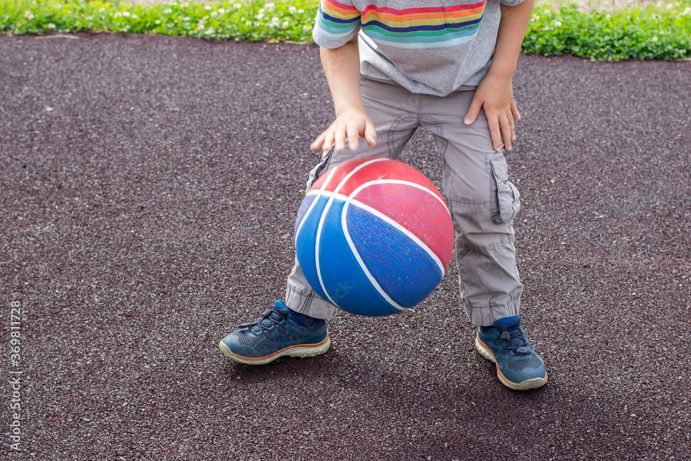 Little boy is playing the basketball outdoor on playground. Child learns to dribble the ball.