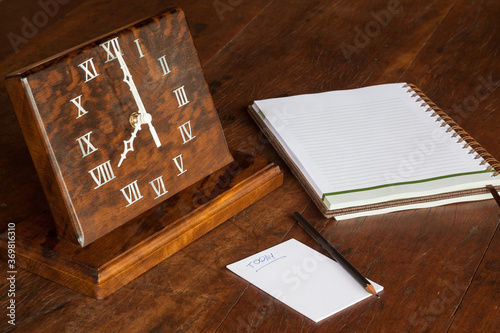 Artisanal wooden clock on the table, with paper to notations and pencil - 08:00 o'clock photo