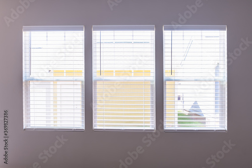 Three windows with closed modern white wood faux window blinds as background.