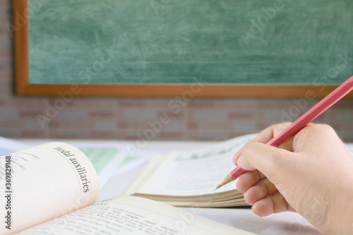 hand holding pencil over blurred textbook on table photo