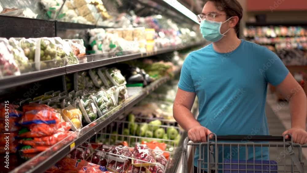 Man in a medical mask pushes shopping cart in a grocery supermarket. Protection from the coronavirus epidemic, increased immunity with fresh fruit. Healthy food for fighting viruses. Man in a medical mask pushes shopping cart in a grocery supermarket. Protection from the coronavirus epidemic, increased immunity with fresh fruit. Healthy food for fighting viruses.