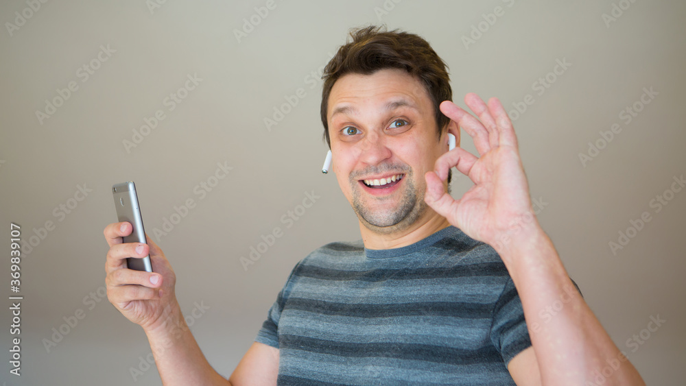 the happy guy inserts a wireless headset into his ear. Man and modern technologies. listen to music. finger pointing