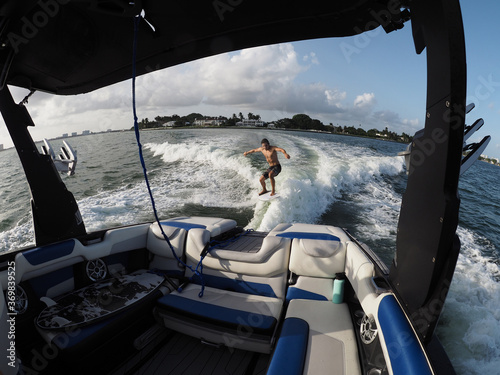 Surfer transfer wave surfing behind boat, interior of boat and seats in the foreground