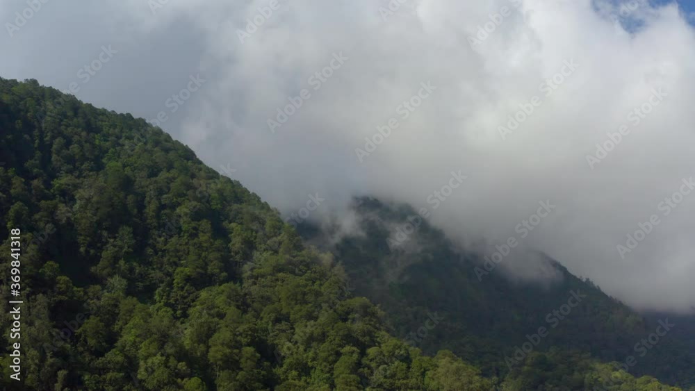 Aerial view of a mountainous tropical rainforest with clouds and mist in the Bedugul resort area of Bali. Drone slow pan right to left Aerial view of a mountainous tropical rainforest with clouds and mist in the Bedugul resort area of Bali. Drone slow pan right to left