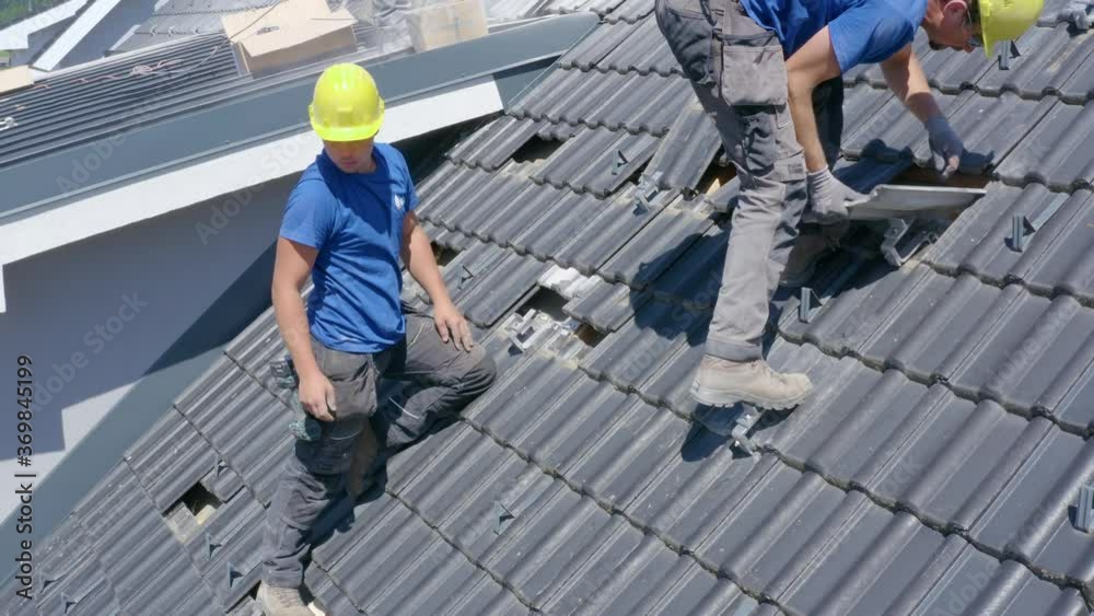 Two man placing tiles in a house roof. Renovation work. Medium shot Two man placing tiles in a house roof. Renovation work. Medium shot