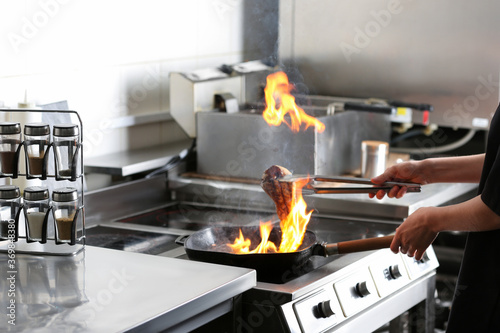 Female chef cooking meat with burning flame on stove in restaurant kitchen, closeup