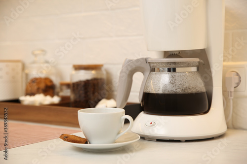 Modern coffeemaker and cup with cookie on table in kitchen photo