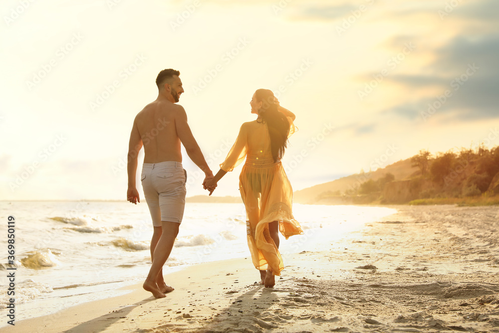 Happy couple walking together on beach at sunset, back view Happy couple walking together on beach at sunset, back view