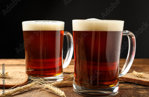 Mugs of delicious kvass, spikes and bread on wooden table against black background
