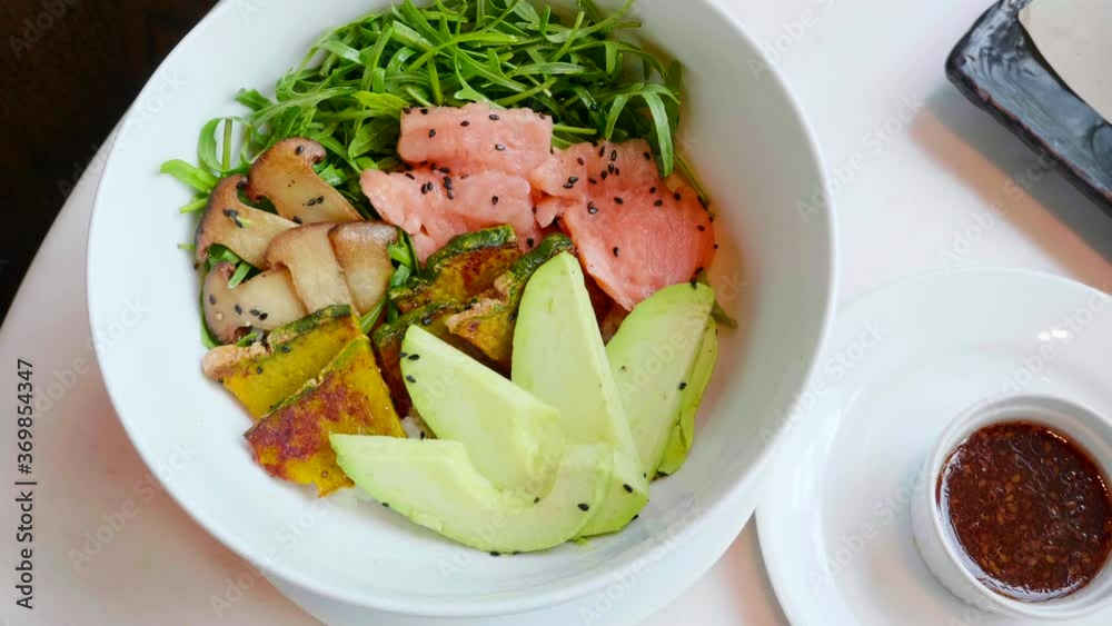 Salmon Poke Bowl with Avocado, Zucchini, Mushrooms and Green Leaves on White Table. Top View. Salad with Raw Fish and Vegetables. Fresh Healthy Delicious Food in Restaurant. Salmon Poke Bowl with Avocado, Zucchini, Mushrooms and Green Leaves on White Table. Top View. Salad with Raw Fish and Vegetables. Fresh Healthy Delicious Food in Restaurant.