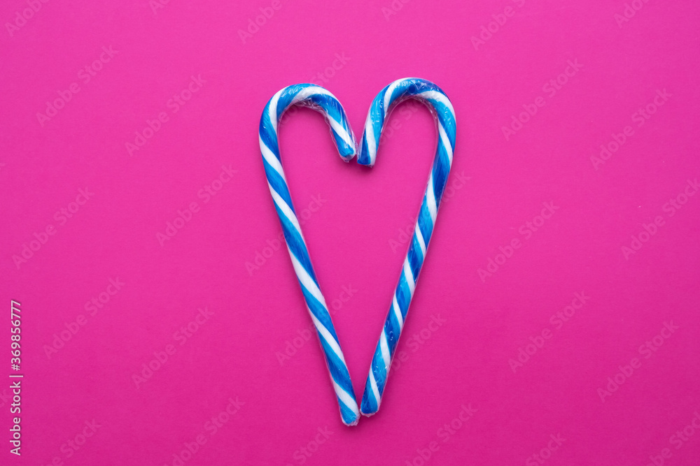 multicolored candy canes in the form of a heart on a pink background, copy space