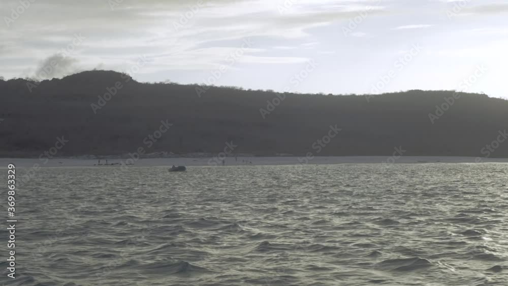 A boat floating on the sea near an island of the Galapagos islands with a hill and beach on the back. A boat floating on the sea near an island of the Galapagos islands with a hill and beach on the back.