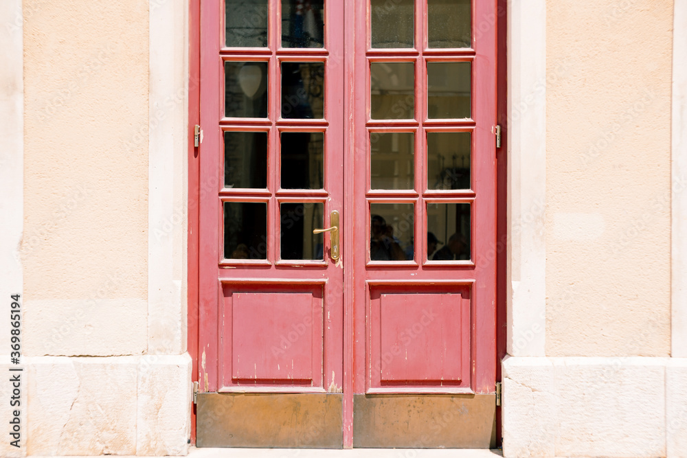 Old red doors with windows in the door with white walls.