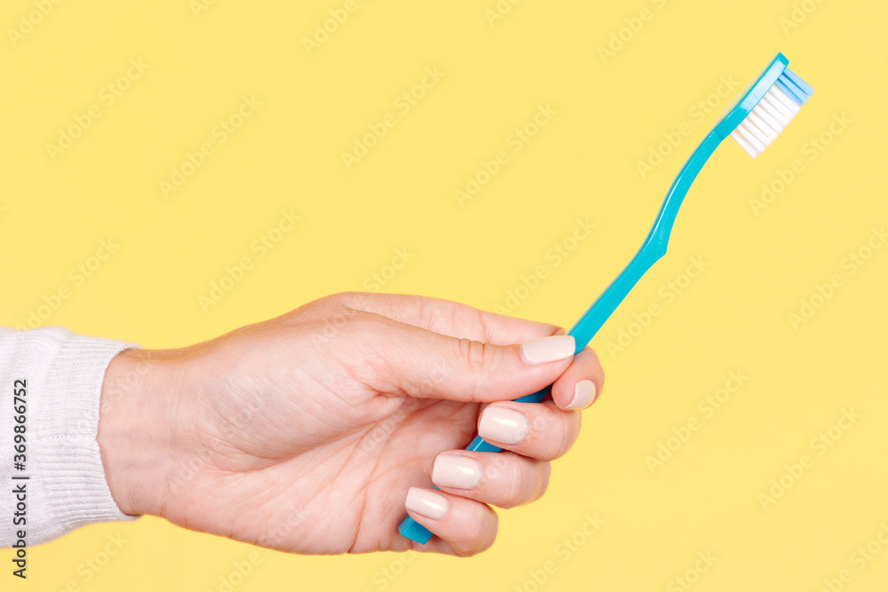 Hand with blue toothbrush, dental care. Isolated on yellow background. Hand with blue toothbrush, dental care. Isolated on yellow background.