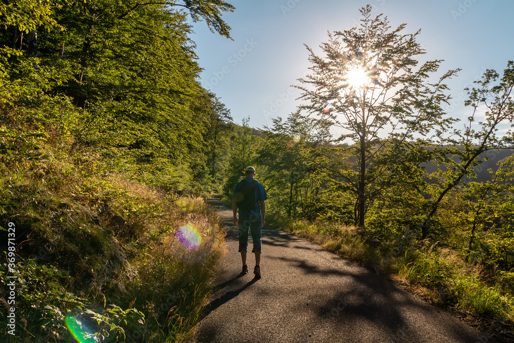 Young man with backpack walking on road in ore mountain forest at sunset. Czech landscape