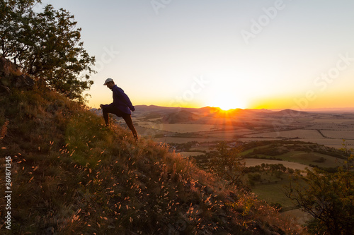 Young man running up to hill in Czech central mountain valley at sunrise. Outdoor landscape