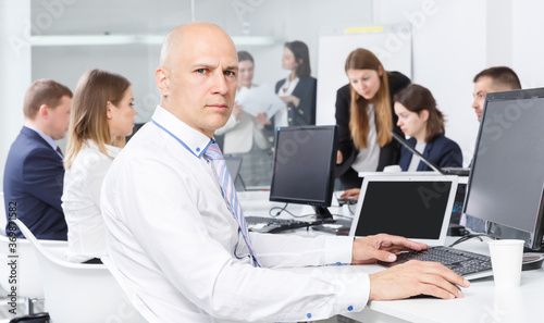 Focused young successful man working with laptop in busy modern open plan office