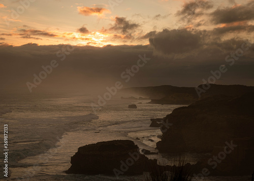 Dramatic scene in the evening, waves coming to shore at sunset, with the coastline made of cliffs in the background