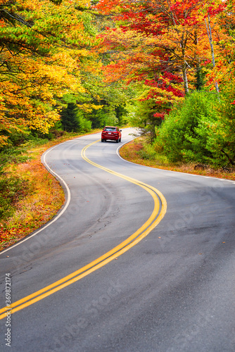 A red car driving through winding road with beautiful autumn foliage trees in New England