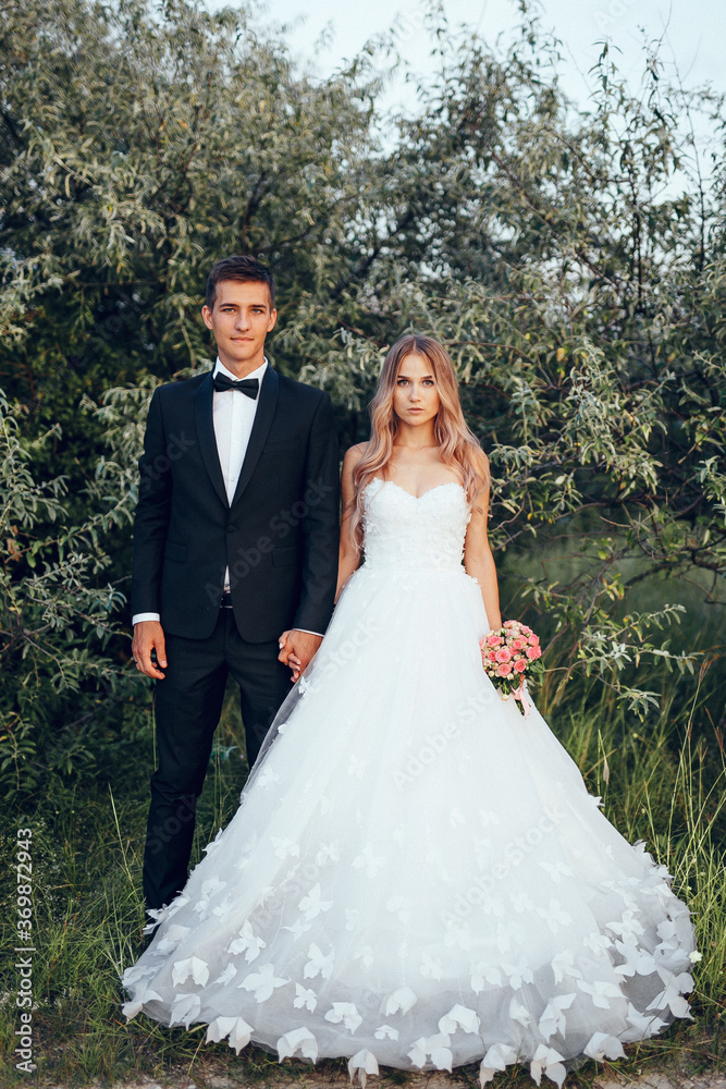 Full length body portrait of young bride and groom enjoying romantic moments outside at sunset in beautiful summer day. Wedding couple. Standing face to face with the green hills on background.