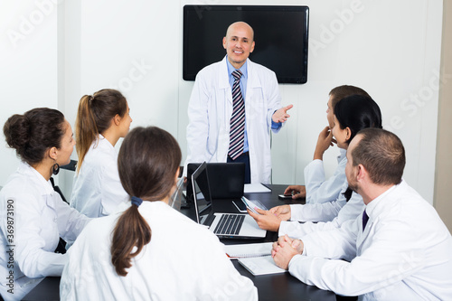 Positive adult specialists in white overalls having discussion of research work