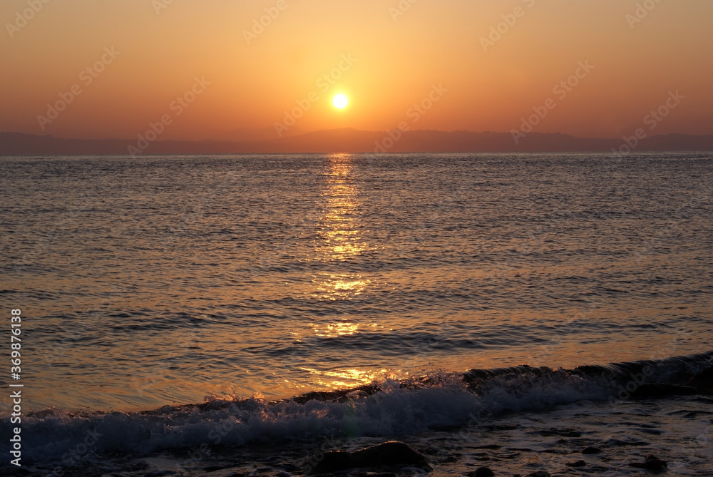 Beautiful dawn over the sea. The sun rises from behind the mountains. Sunny path on the water. Light wave and swell on the surface of the water