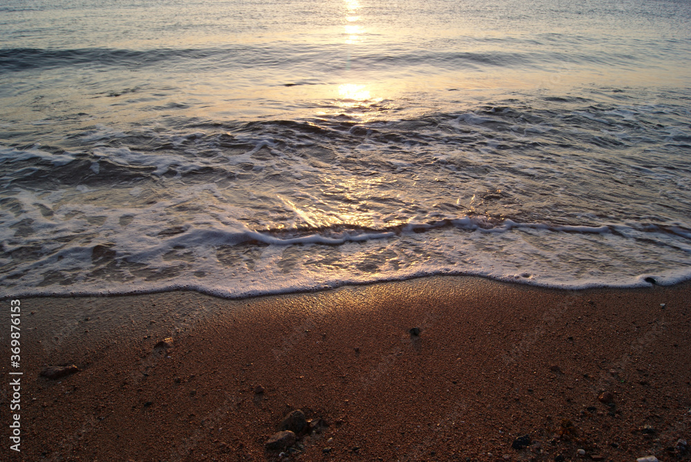 Calm sea wave on a sandy beach at sunrise. Sunrise on the sea. Sea foam. Wave edge on wet sand. Solar path on the sea surface Calm sea wave on a sandy beach at sunrise. Sunrise on the sea. Sea foam. Wave edge on wet sand. Solar path on the sea surface