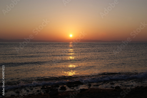 Beautiful dawn over the sea. The sun rises from behind the mountains. Sunny path on the water. Light wave and swell on the surface of the water