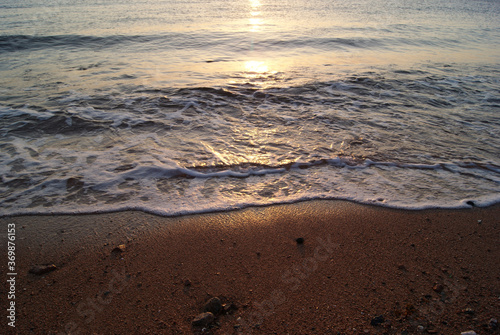 Fototapeta Naklejka Na Ścianę i Meble -  Calm sea wave on a sandy beach at sunrise. Sunrise on the sea. Sea foam. Wave edge on wet sand. Solar path on the sea surface