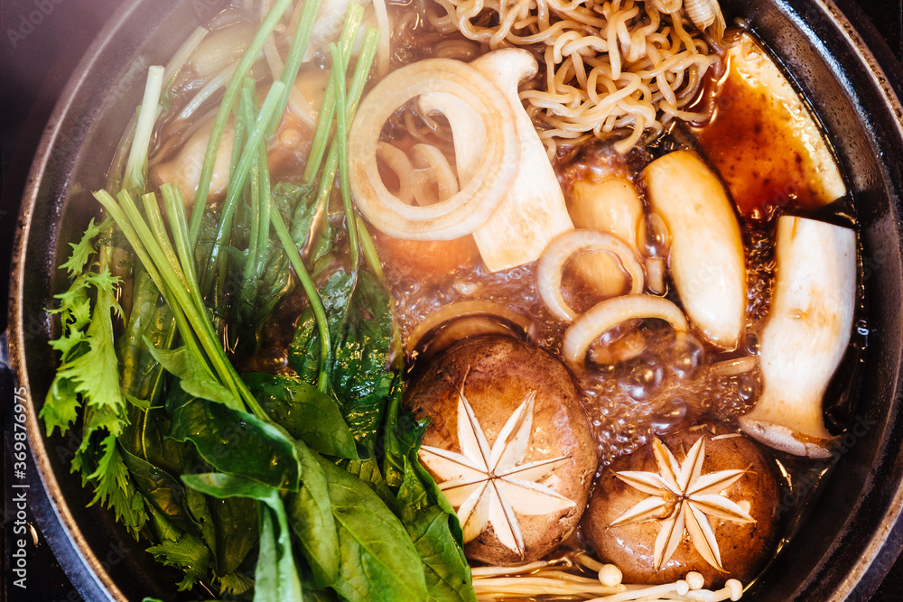 Φωτογραφία Close up top view of Sukiyaki hot pot with boiling vegetables including cabbage, konjac noodle, onion, carrot, shiitake, enokitake and tofu in Shoyu sauce soup