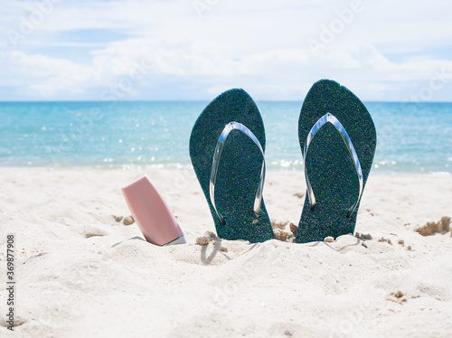 Flip flops and sunsceen on sand beach with blue sea.