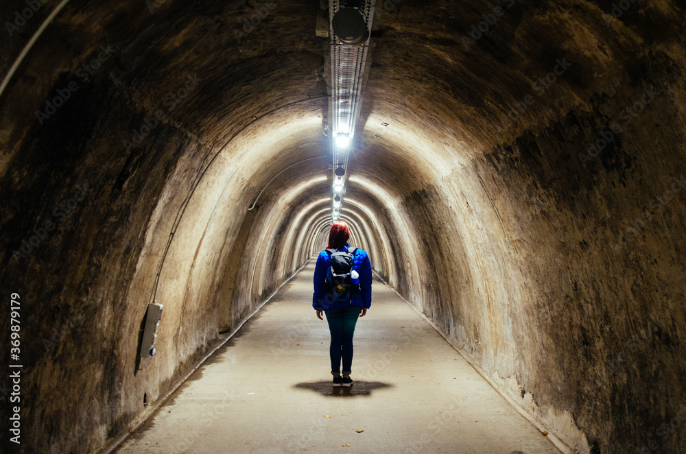 A young adult woman standing in front of an empty pathway inside Gric Tunnel in Zagreb, Croatia, illuminated by fluorescent lamps.