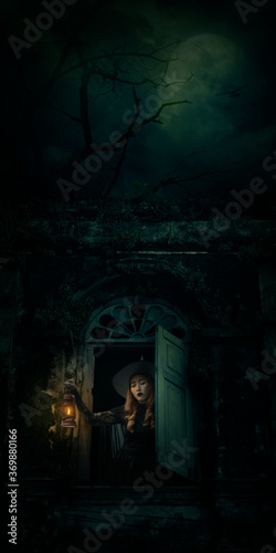 Halloween witch holding ancient lamp standing in ancient window building over dead tree  birds  full moon and spooky cloudy sky  Halloween mystery concept